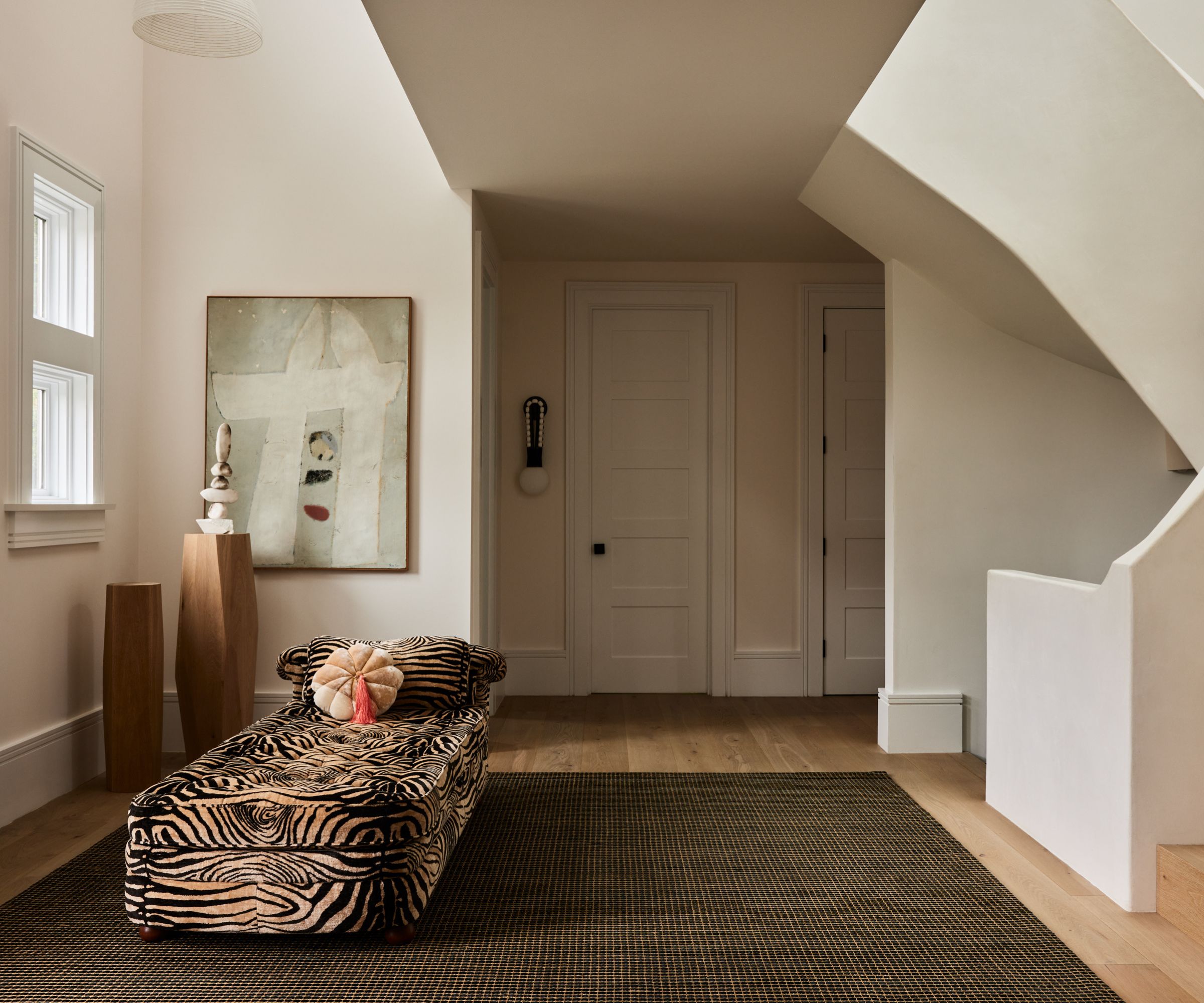 Entryway with spiral staircase, large olive green rug on wooden floor, tiger print daybed with velvet pink cushion and modern abstract painting in the background