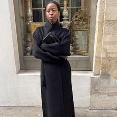 Sylvie wears a black wool coat and a clutch.