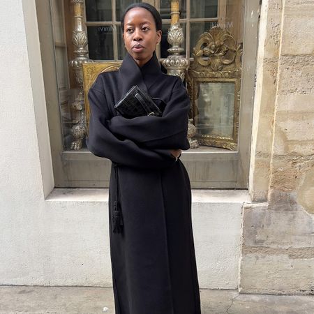 Sylvie wears a black wool coat and a clutch.