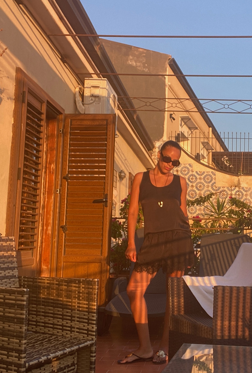 How to pack for Italy is shown in a picture of a fashion editor wearing a black silk tank, black lace shorts, black flip flops, and black sunglasses