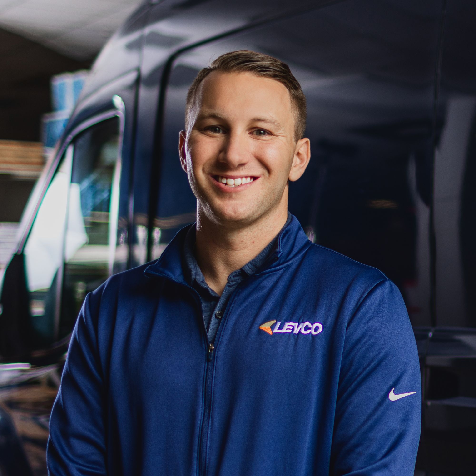 A picture of Scott Levene - a man wearing a blue fleece smiling in front of the camera, standing in front of a blue van
