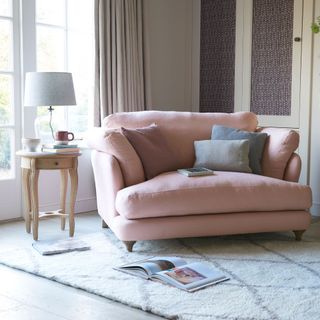 pink loveseat in living room with berber room and lamp on side table