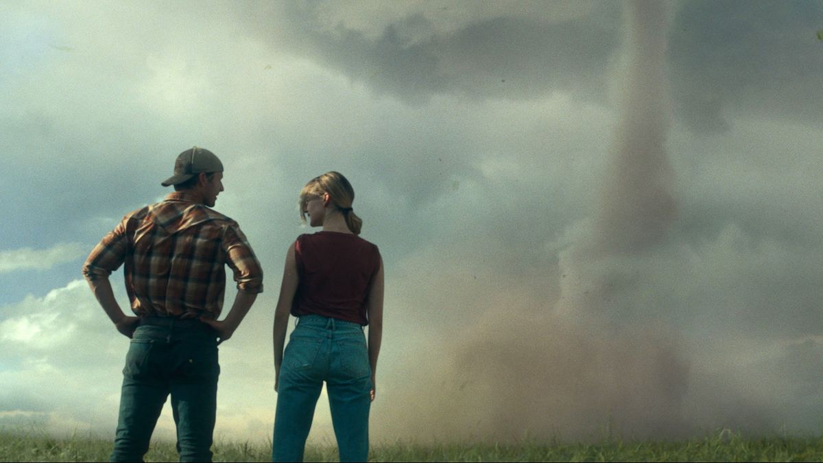 Glen Powell and Daisy Edgar-Jones facing away from the camera looking at a Tornado in &quot;Twisters&quot;