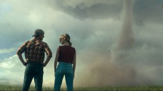 Glen Powell and Daisy Edgar-Jones facing away from the camera looking at a Tornado in 