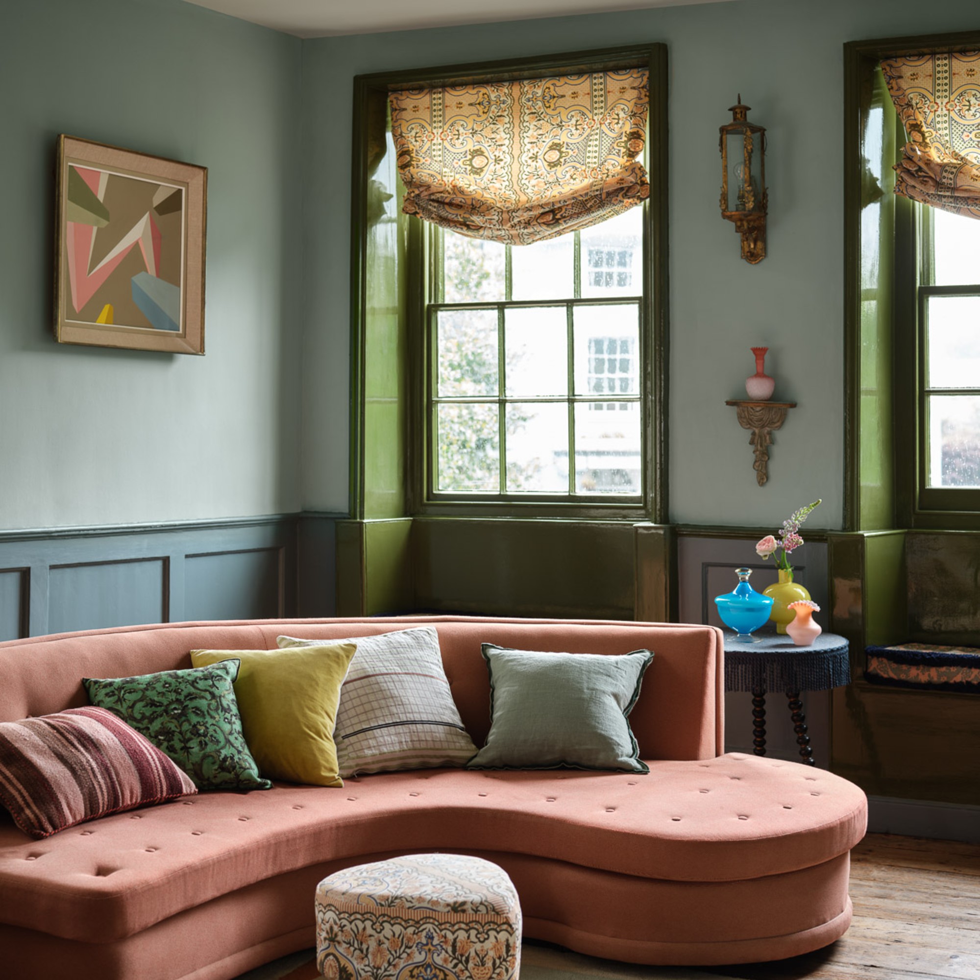 A blue-painted living room with a curved pink sofa and window frames painted green
