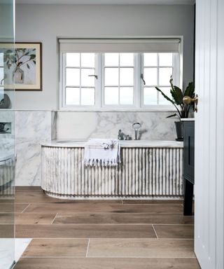 Marble bathroom with fluted bath, dark wooden flooring