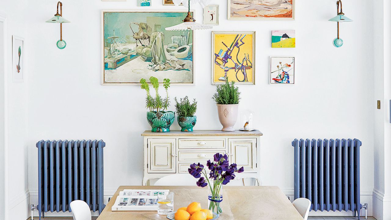 Blue painted radiators in dining room of large home with gallery wall and large wooden dining table