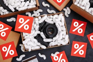 Cardboard box with camera and protective foam pads inside on black background with red percentage symbols scattered around