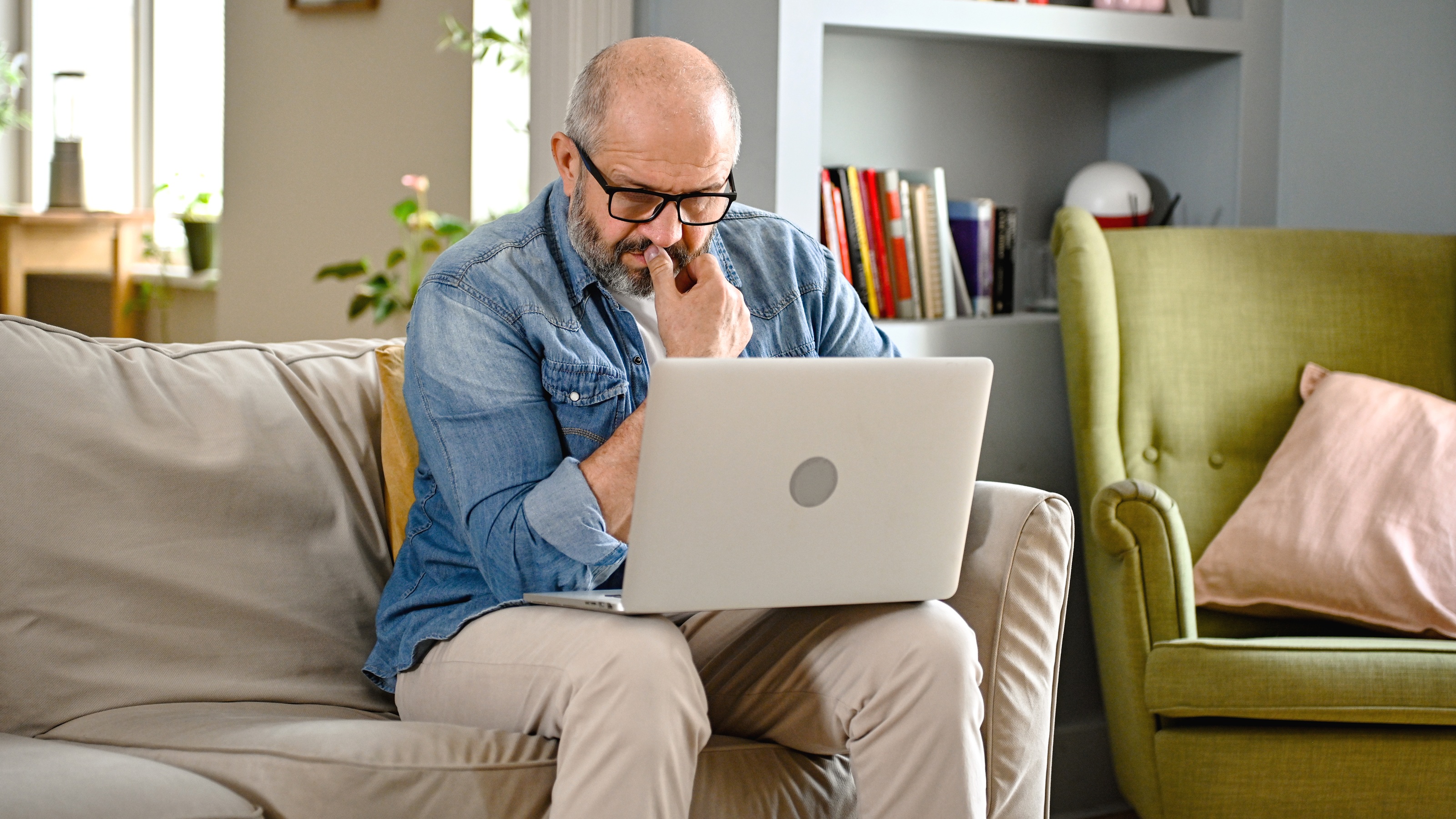 An older man stares intently at his laptop while sitting on his sofa.