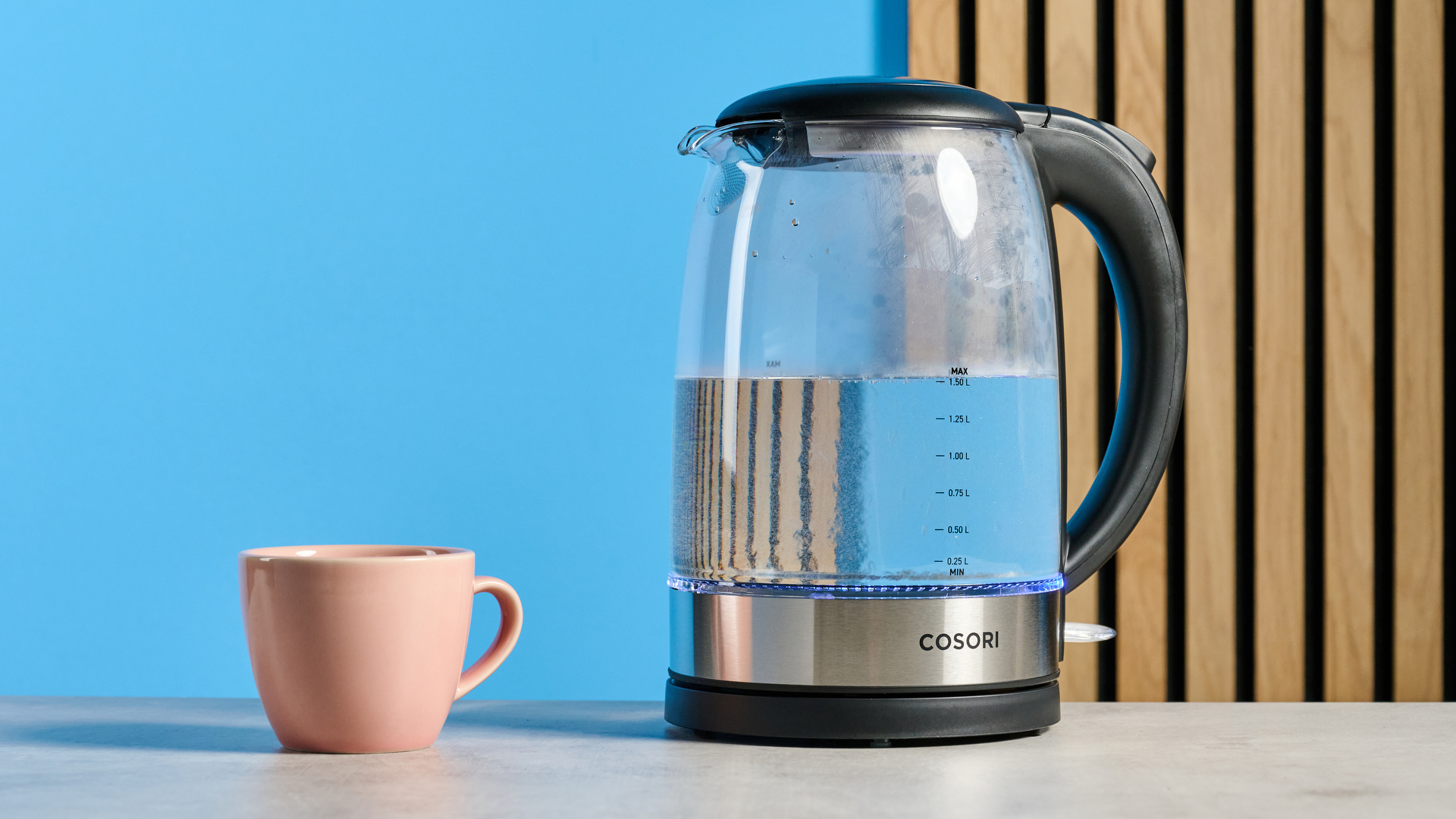 Cosori Electric Glass Kettle photographed in front of a blue background.