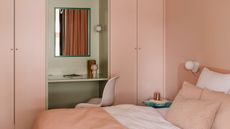 soft sun-baked pink color drenched room with matching bed linen and a sage green vanity area with a pink chair and mirror 
