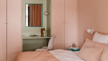 soft sun-baked pink color drenched room with matching bed linen and a sage green vanity area with a pink chair and mirror 