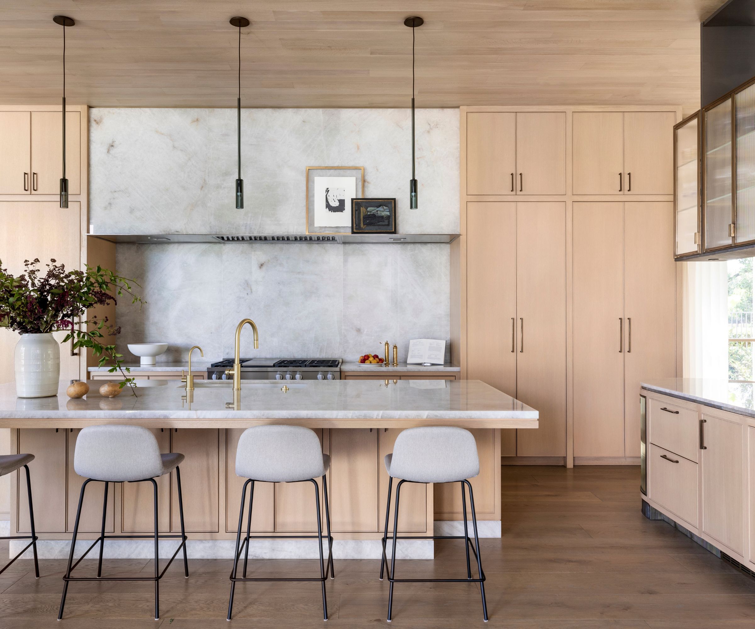 modern kitchen with light wood custom cabinets, large kitchen island with light gray bar chairs
