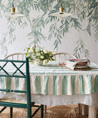 Dining room with white and green botanical wallpaper, green and white striped tablecloth, green dining chair, vase of whit flowers