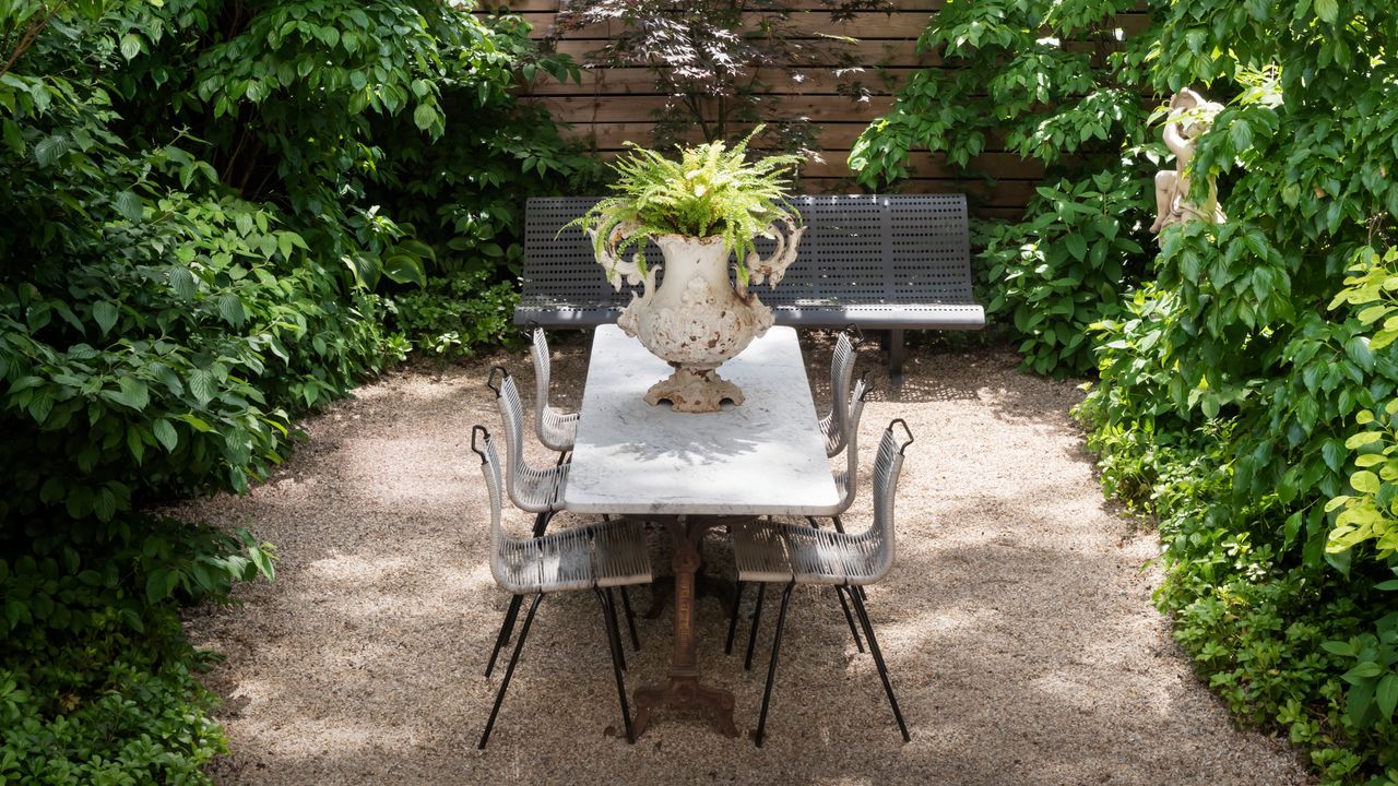 Patio with gravel underfoot, iron table and chairs and lush green planting