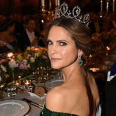 Princess Madeleine wearing an off the shoulder green gown and diamond tiara sitting at a dinner table with flowers and candles