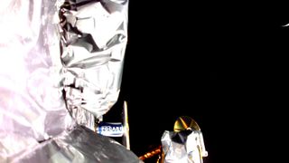 photo showing the silvery insulation of a spacecraft and the blackness of space in the background, with a possible sliver of earth in the upper right corner.