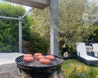 Weber Smokey Joe BBQ cooking burgers in garden with hot tub and sun loungers behind