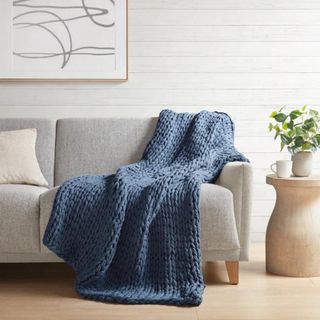 A blue chunky knit throw blanket in a neutral living room