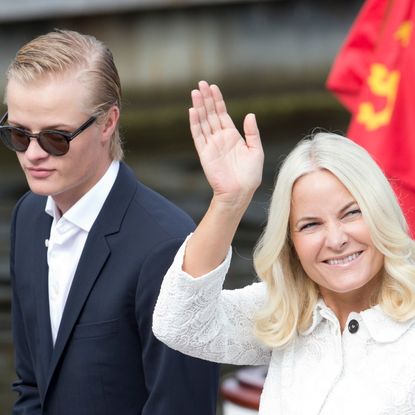 Marius Borg Hoiby wears sunglasses and has slicked back blond hair, and his mother, Crown Princess of Norway Mette-Marit, wears a white jacket, has blonde hair, and waves