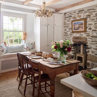 Modern farmhouse style dining room with rustic wooden table, exposed stone walls, log burner and window seat