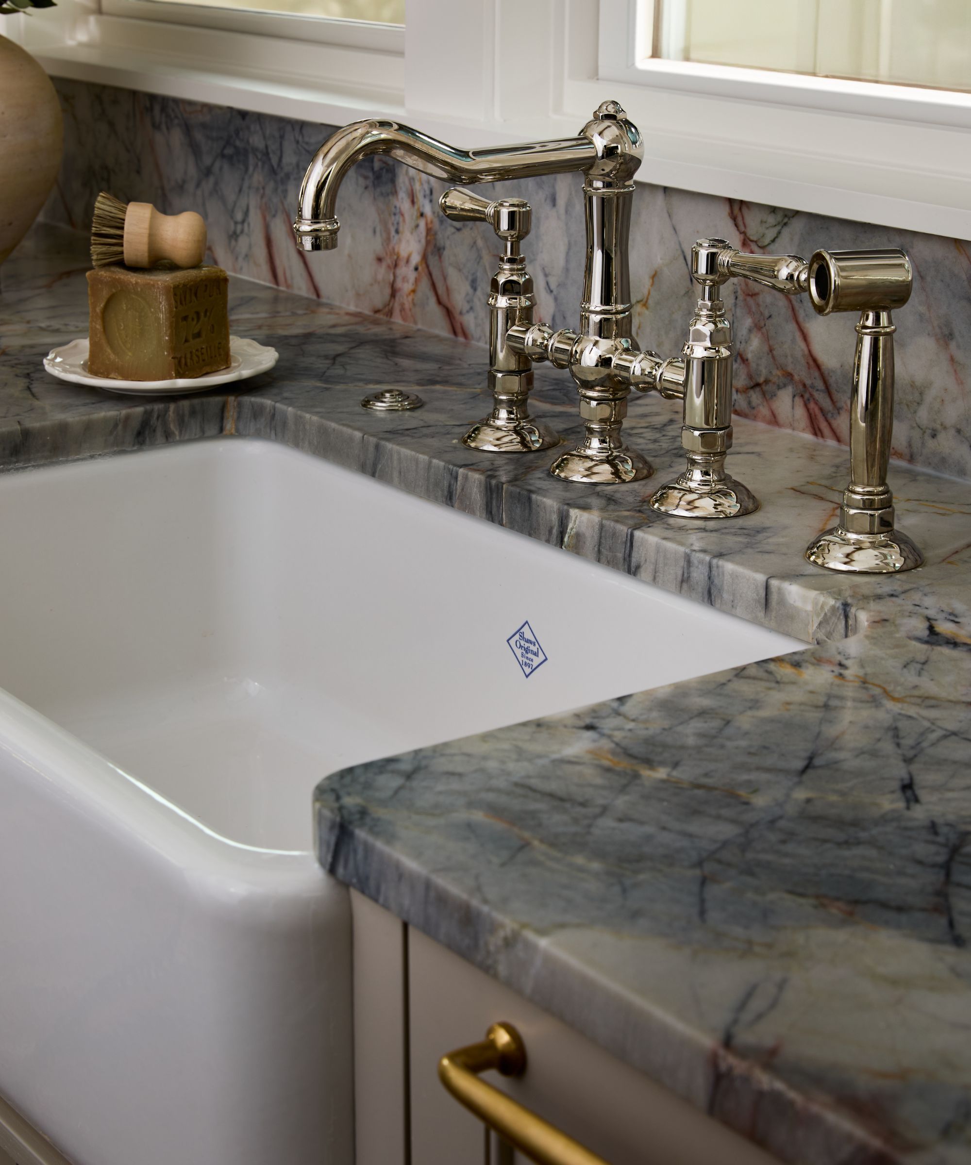 neutral kitchen with a blue veined marble countertop and backsplash, silver traditional vintage style taps and a farmhouse butler sink