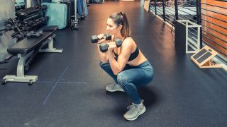 Woman performs squat in gym with dumbbells