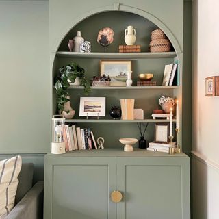 An arched bookcase in a living room painted in a sage green shade matching the adjacent wall