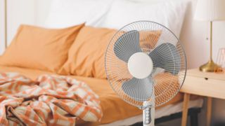 An electric fan in front of a bed with orange sheets