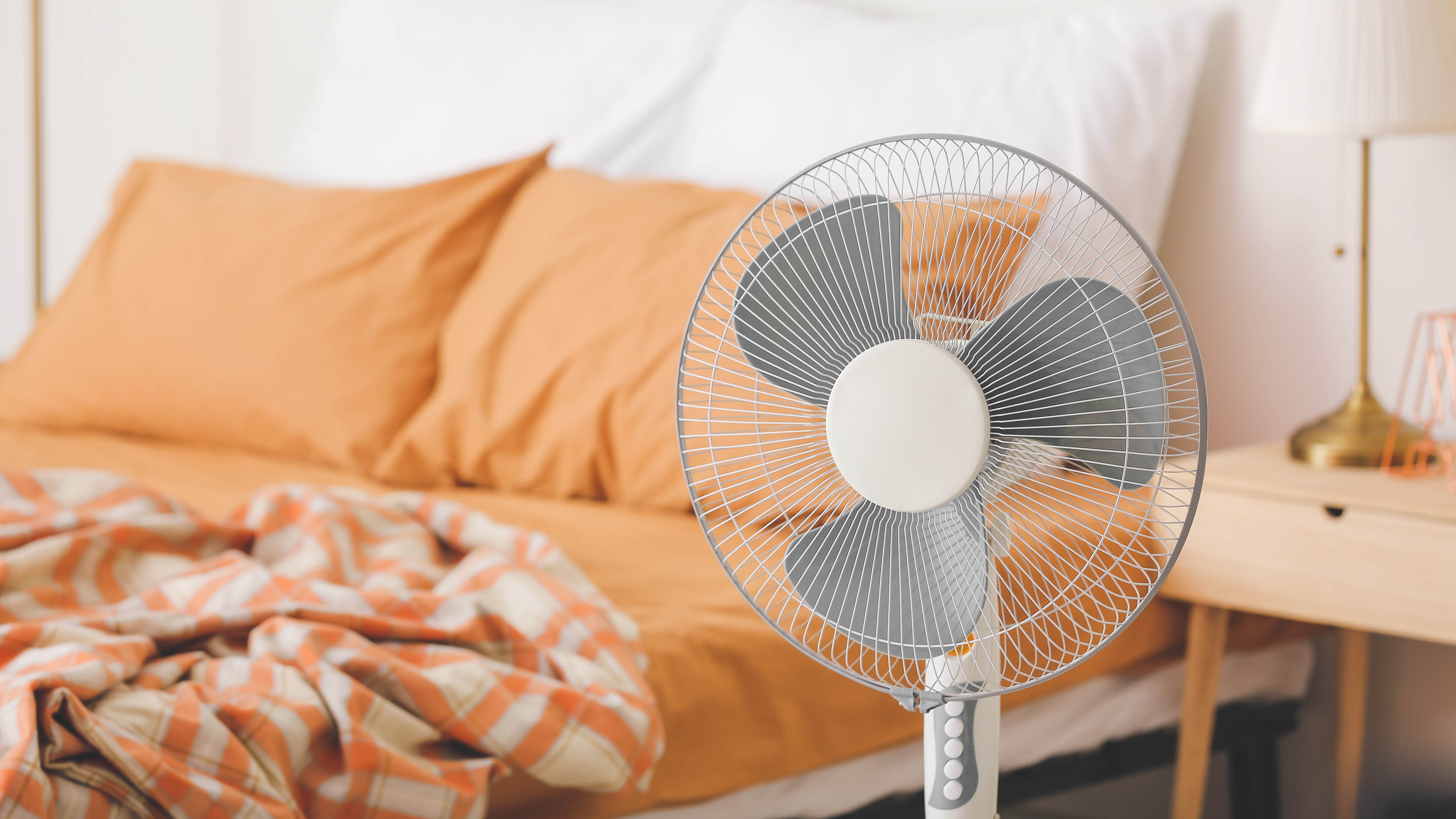 Электрический вентилятор перед кроватью с оранжевыми простынями
