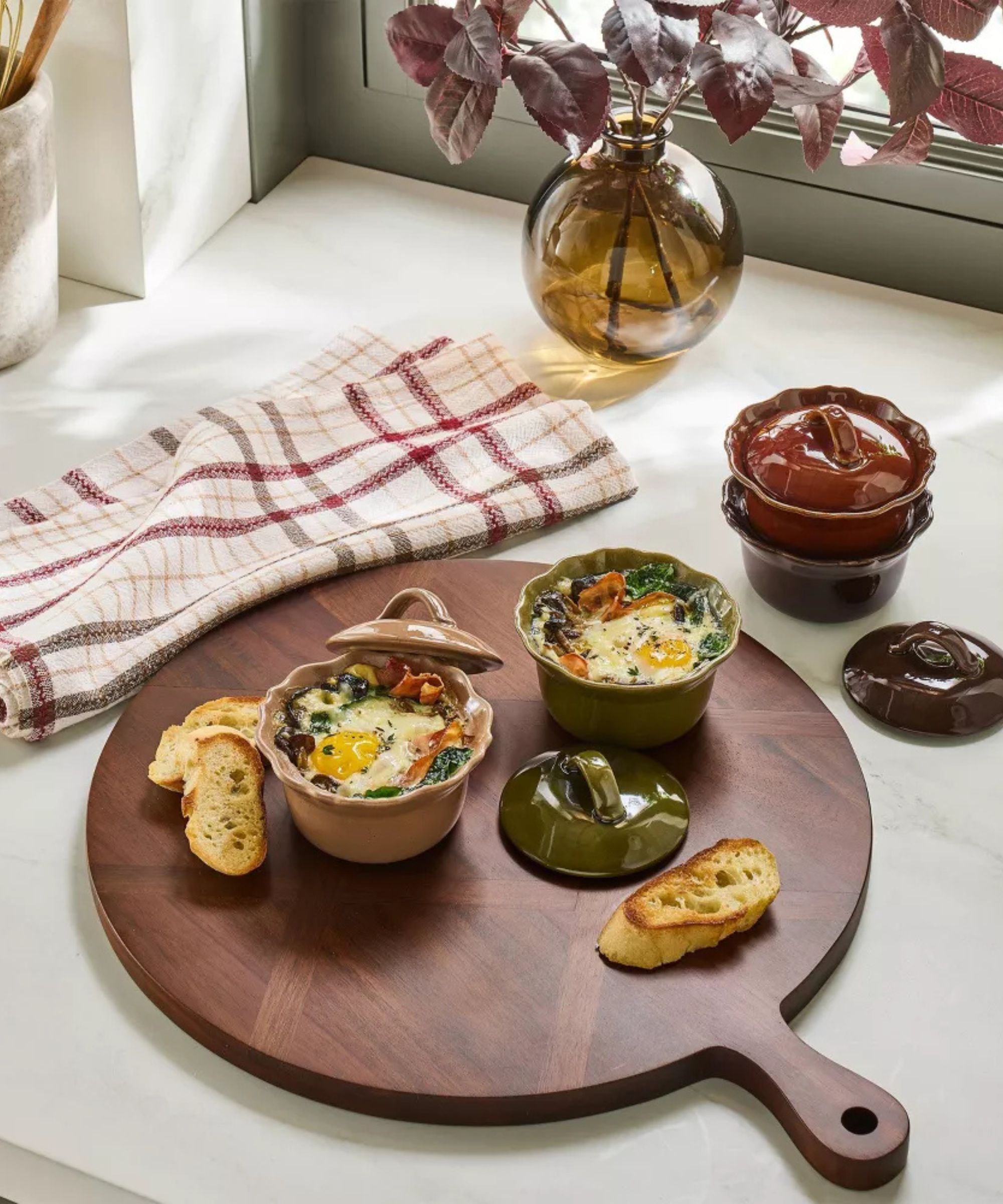 Round wooden serving board with pink and green pinch bowls and a red tartan dish towel