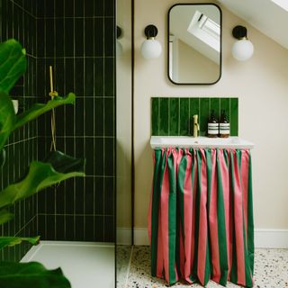 A bathroom with a green tiled shower and a sink with a striped curtain