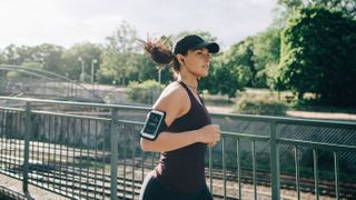 Cyber Monday running headphones deals. Here, a woman running with earbuds in that are connected to a smartphone on her arm.