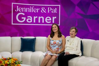 Jennifer Garner sitting on a white sofa with her mother Pat Garner with a purple background reading "Jennifer and Pat Garner"