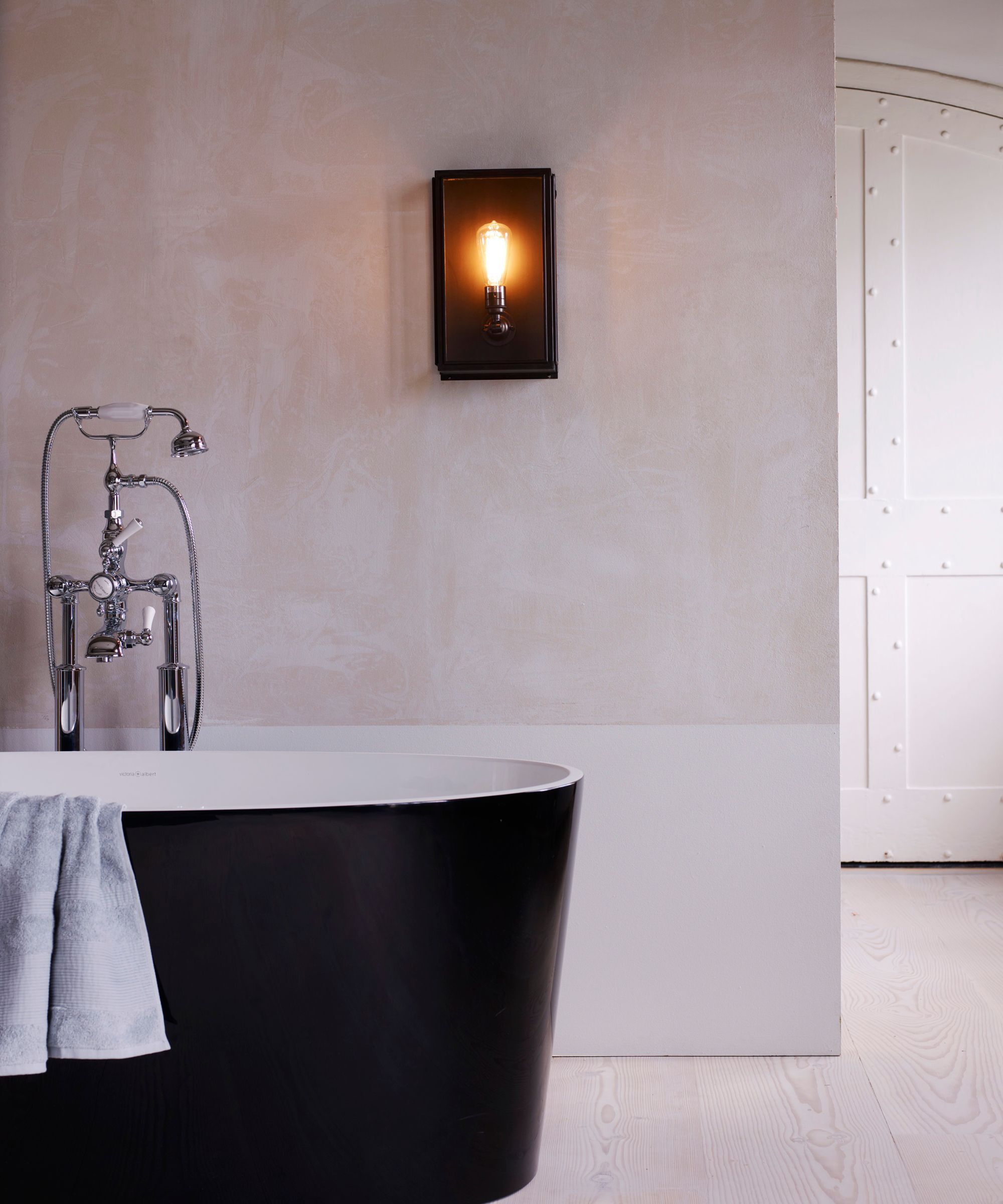 A black bathtub with a black box light on the wall behind.