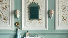 Small bathroom wall paneling ideas look so smart. Here is a bathroom with white wall panels with brown bird wallpaper, teal walls, two white wall sconces, a white standing basin, and a light blue towel