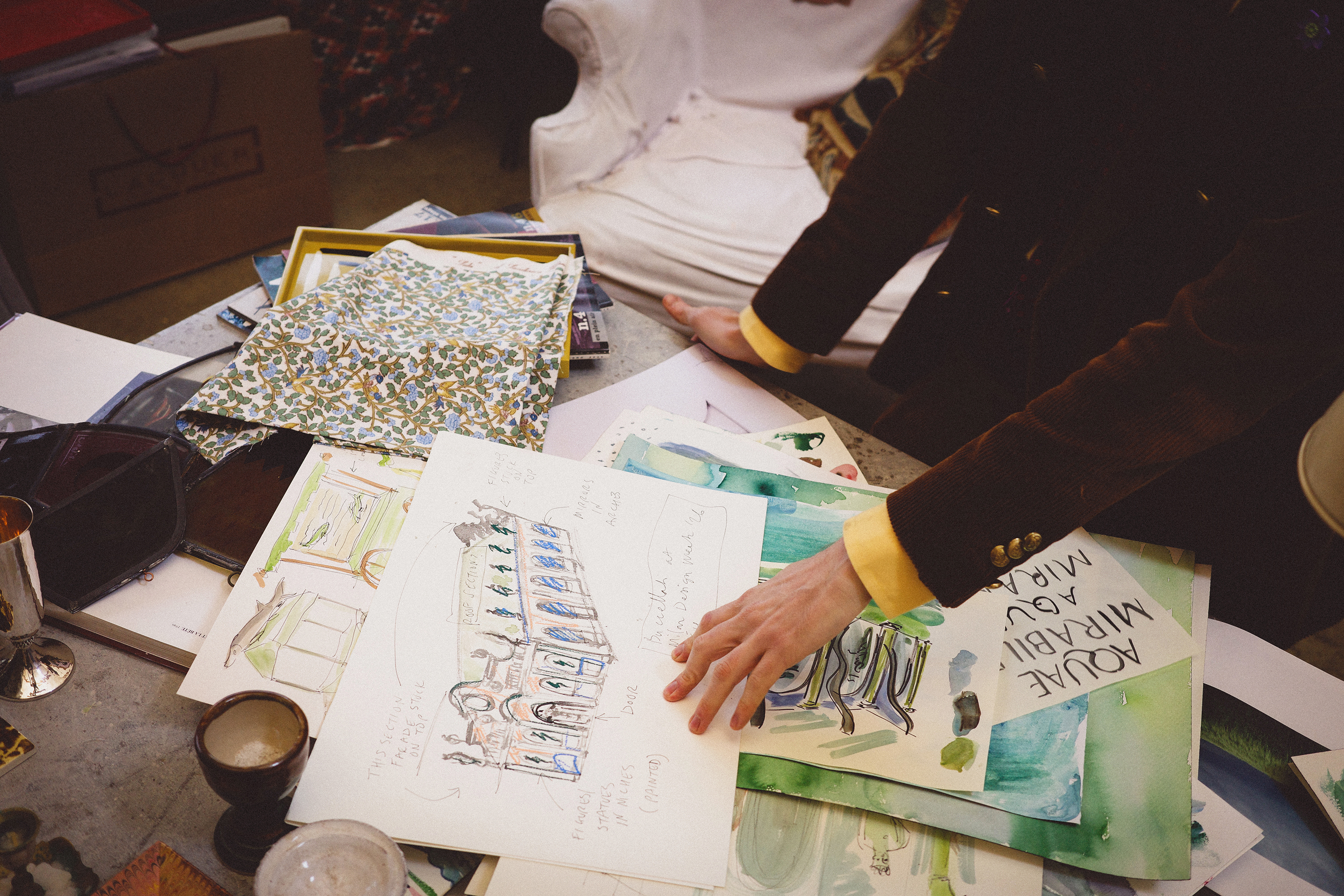 Luke Edward Hall's hands captured from above near some hand-painted waterpaint sketches.