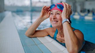 Happy woman smiling at edge of swimming pool wearing goggles and swim cap