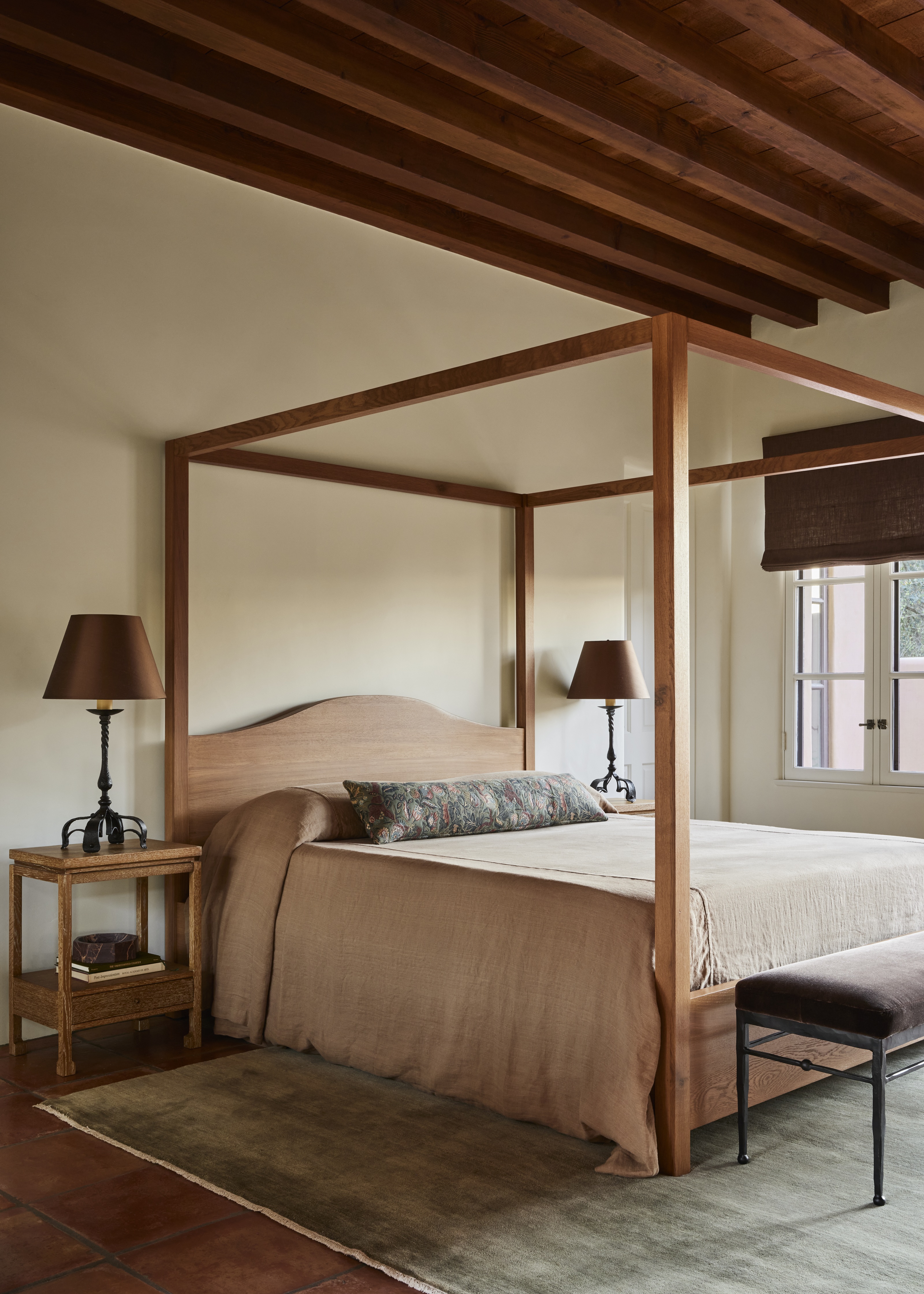 a rustic bedroom with beams, a wood four poster bed, and matching table lamps