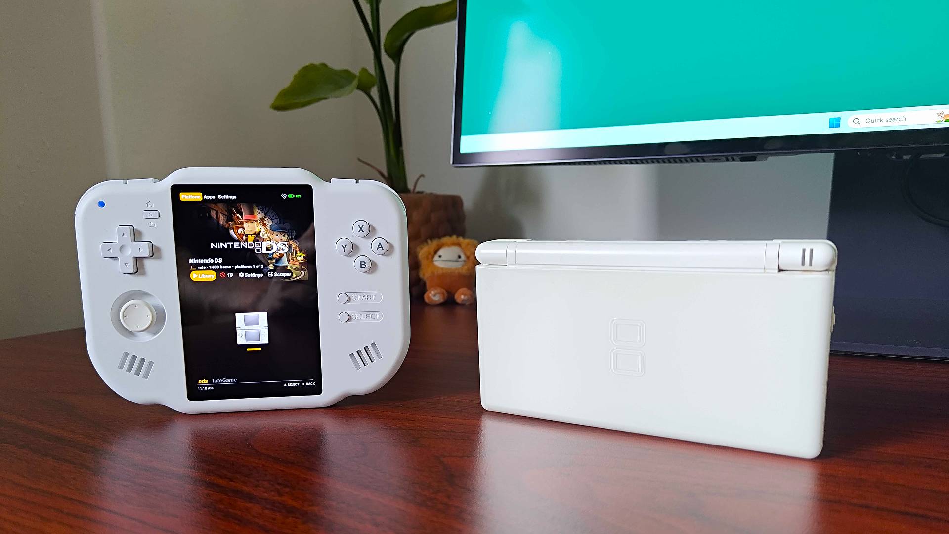 MagicX Zero 40 on left and Nintendo DS Lite on right standing upwards on woodgrain desk next to plant and monitor.