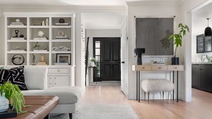 Light gray styled hutch in open plan space with light wooden floors, facing the front door with black kitchen visible on the right