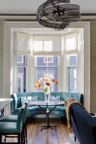 dining room/living space with window seat, blinds at bay window, sculptural pendant light, blue couch, stripe throw, black round table, poppies in vase