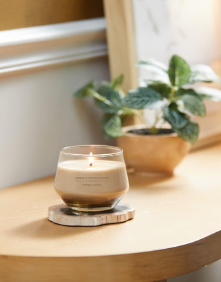 beige candle in a glass container on a shelf with a plant behind