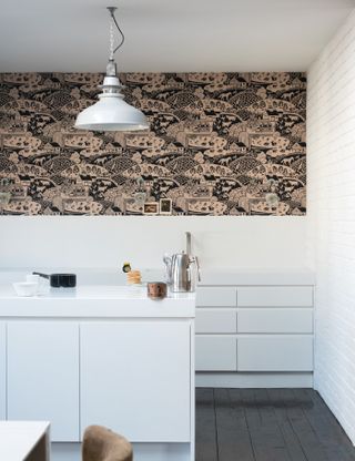 A white kitchen with black and blush pink / peach kitchen wallpaper with white pendant light