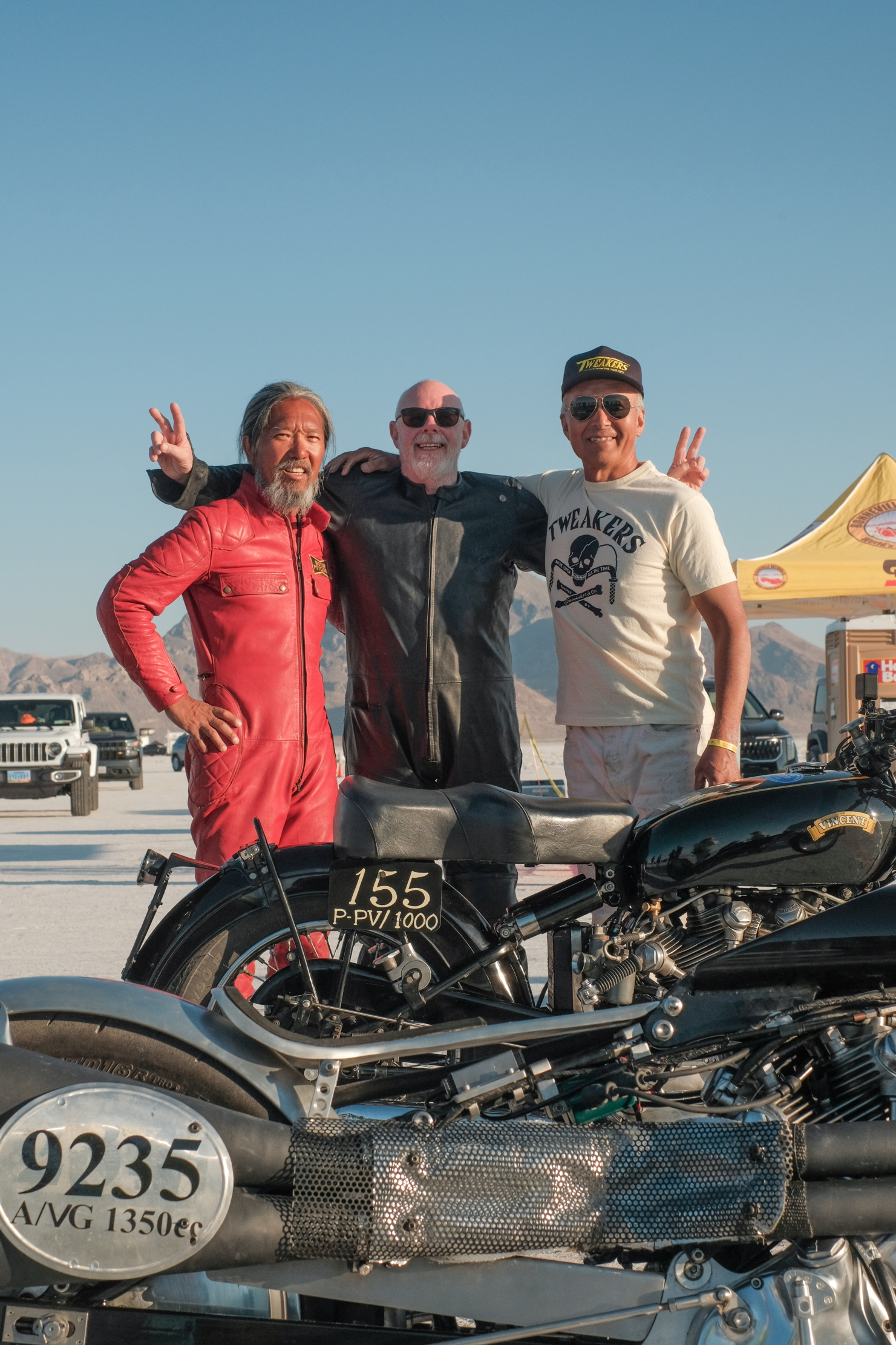 Three competitors stand over a motorbike