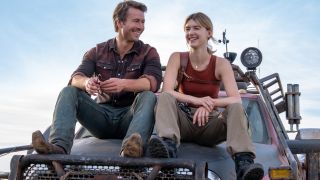 Glen Powell and Daisy Edgar-Jones smiling together while sitting on top of a truck&#039;s hood in Twisters.