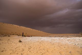 A dark cloud lingers overhead as archaeologists survey and map the Al Wusta site.