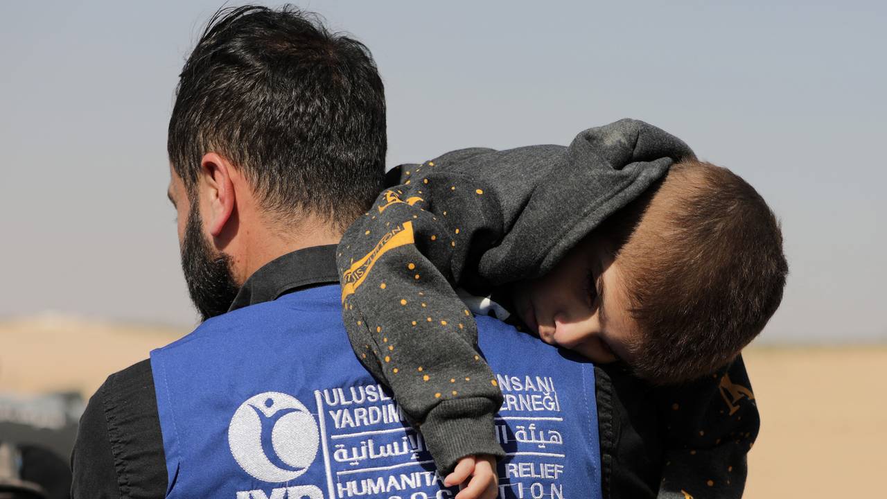 A relief worker carries a child across the border into Syria