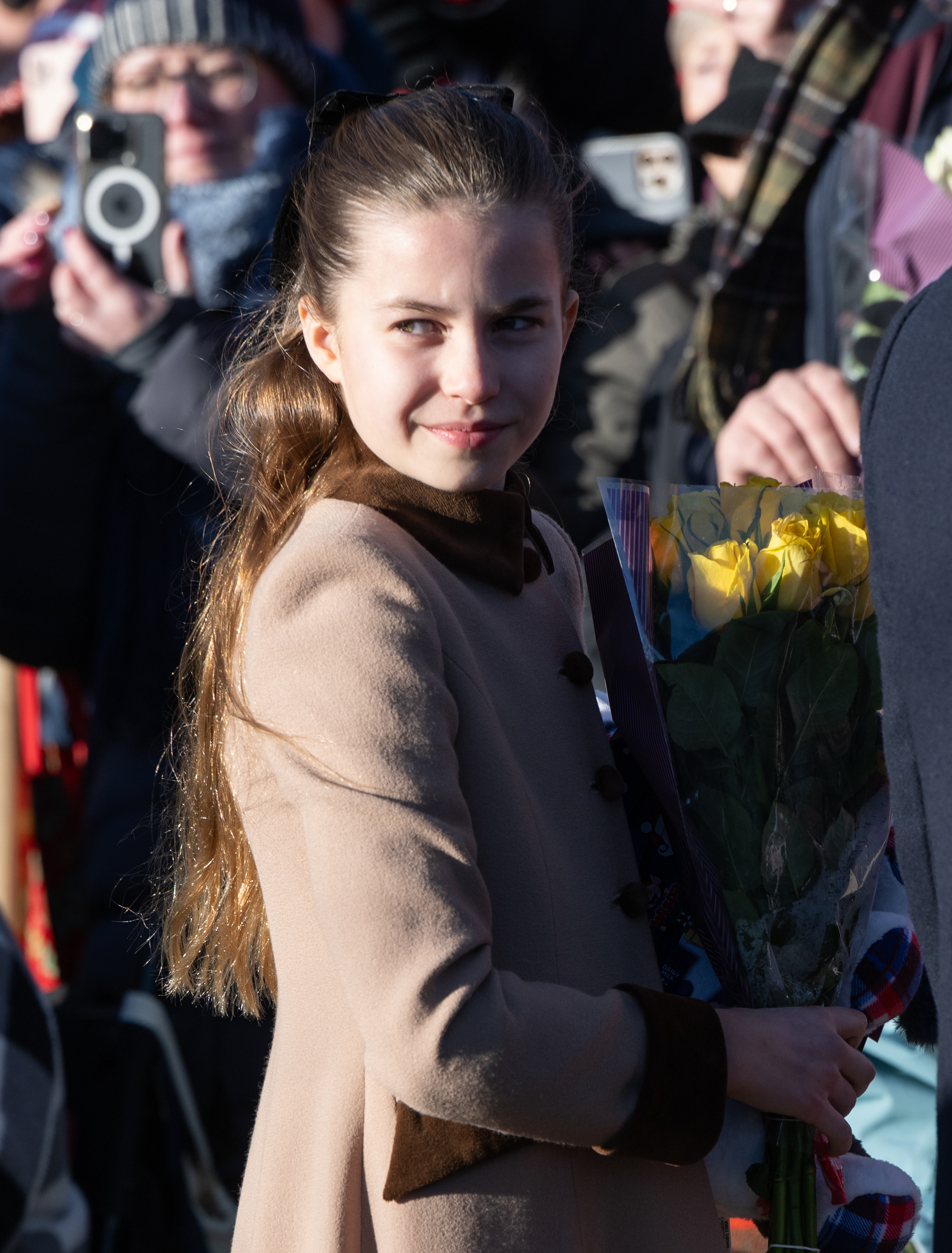 Princess Charlotte wearing a brown coat holding yellow roses