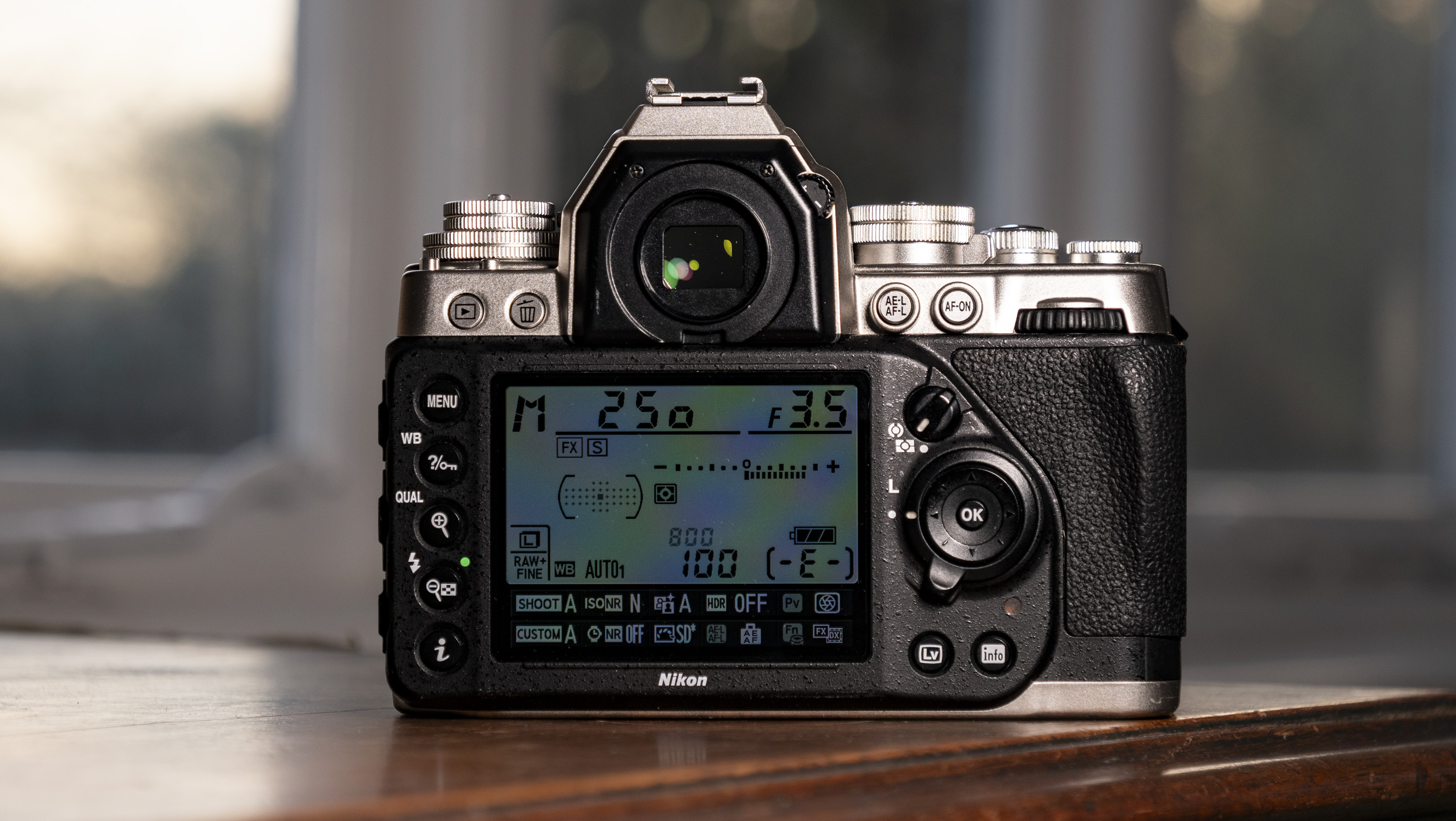 Nikon Df DSLR camera on a wooden surface by large window, with dusk light